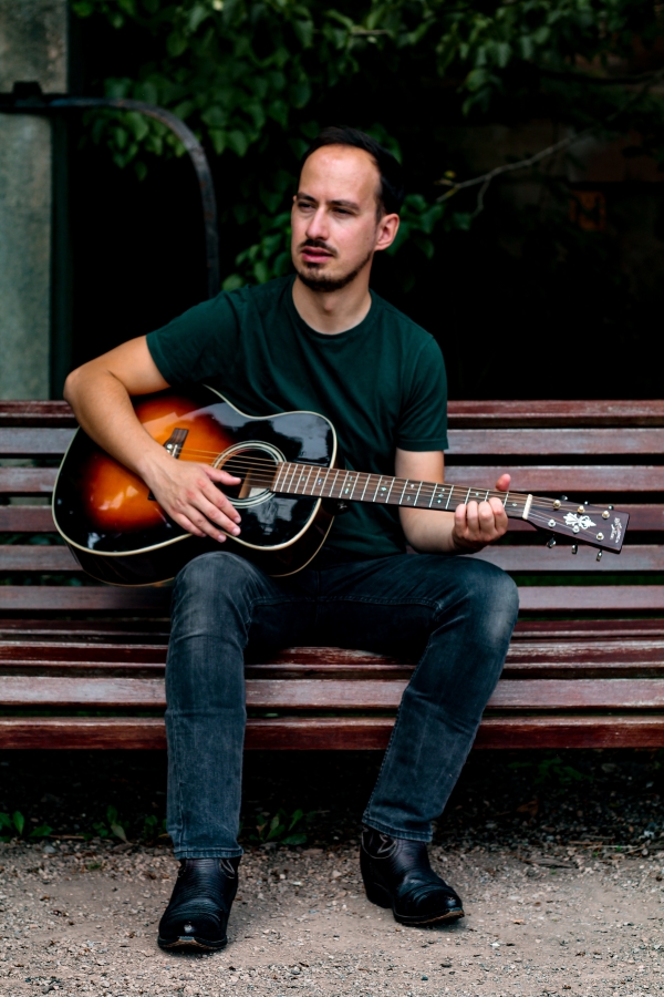 Ben Atkinson sitting a bench playing guitar